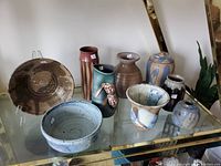 Nine pieces of handmade ceramics including bowls, vases, and jars displayed on a glass shelf.