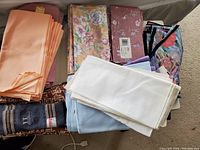 Multiple stacks of cloth table napkins in various colors and floral patterns, folded and overlapping on carpeted floor.