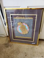 Framed mixed media 3D art with abstract shapes in gold, pink, and blue on gray background, gold frame, dark mat, approximately 18x24 inches
