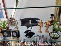 Shelf with varied decorative arts: 2 rectangular perfume bottles, 2 wooden artist figures, small woven sculpture, black ceramic plate, resin statue