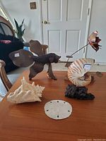 Full view of all six ocean themed decorative pieces arranged on a wooden table including shells, brass sculptures, and a plant on driftwood.