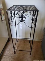 Metal plant stand with detailed scrollwork and fleur-de-lis motifs, lattice top surface, and four supporting legs.