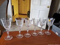 Six crystal wine glasses arranged in a row on wooden table, intricately cut with faceted and diamond shaped etched design, clear and shiny