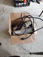 Top view of a cardboard box containing four used surge protectors with cords tangled together.