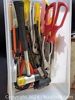 Top view of a collection of used hand tools in a white box showing hammers, pliers, scissors, files, and wire cutters.