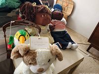 Photo showing two black dolls, a plush dog, and a green parrot mobile on a table.