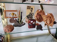 Shelf displaying various art objects including leather sculptures, ceramic masks, woven baskets, a book, and small sculptures.