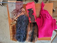 Top view of a wooden surface displaying 3 fur collars, a bright pink knitted hat, and a maroon and black patterned scarf.
