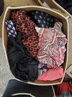 Box containing several scarves in various patterns including leopard print, star pattern, paisley, and solid black and pink scarves.