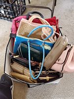 Photo showing top view of multiple assorted women's purses packed in a container, including woven, leather, and fabric styles.