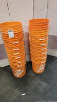 Two stacks of orange plastic Home Depot buckets without lids stacked against a wall.