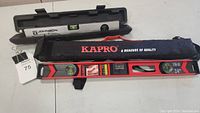 Two construction levels with cases, one Johnson Level & Tool in a black hard case and one Kapro level in a black fabric bag.