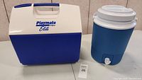 Photo showing blue and white Playmate Elite cooler and blue water dispenser cooler with white lid and spigot