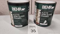 Two cans of Behr Alkyd Semi-Gloss Enamel paint placed side-by-side for size and label visibility.
