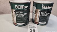 Two cans of Behr Alkyd Semi Gloss Enamel Interior/Exterior paint, showing front labels and size information.