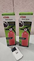 Two boxed new Kidde Home Series fire extinguishers displayed side by side on a surface with a lot tag.