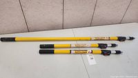 Three Auto-Lock yellow extension poles laid out horizontally showing full length and labels with black locking mechanisms.