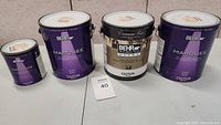 Four Behr paint cans shown on surface with lot number card beside them