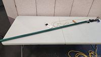 Full view of the green extendable pole branch cutter laid out on a white table showing its length and build.