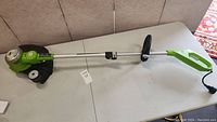 Full view of Greenworks electric string trimmer showing cutting head, shaft with adjustable handle, and trigger handle with power cord.