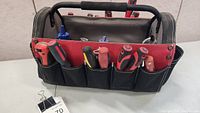 View of the Husky tool bag showing screwdrivers in exterior pockets and the bag's black and red design with padded handle.