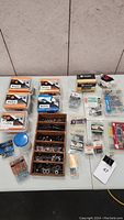 Overview of multi-purpose nails, screws, bolts, washers and fasteners lot on table including wooden organizer, multiple plastic containers, and new unopened packages.