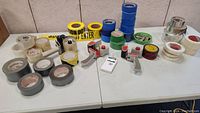 Overview of the entire lot displayed on two white tables showing various tape rolls and tape dispensers.