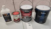 Four paint and solvent containers including Behr Premium Garage Floor Paint, Behr Marquee Satin Enamel Paint, Varasol solvent, and clear coat labeled Varnishettone.