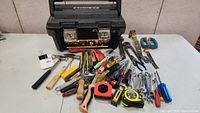 Wide shot showing the black Stanley 20-inch Pro Tool Box and an array of tools spilled out in front of it on a white surface.