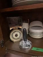 Photo showing mechanical kitchen scale with clear container and white analog kitchen scale along with a plastic handled pastry cutter wrapped in plastic