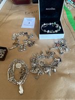 Five bracelets displayed on paper surface including Pandora in box and four chain charm bracelets