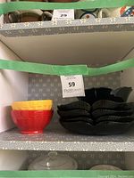 Red and yellow ceramic bowls stacked next to black ceramic plates and bowl on a shelf.