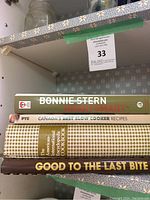 Photo showing a stack of four vintage cookbooks on a shelf with visible titles and cover designs.