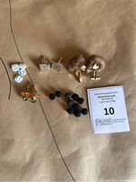 Photo showing various vintage cufflinks arranged on tan surface including white oval, gold-green stone, silver square textured, faux fur pom-pom, and black fabric knot styles.