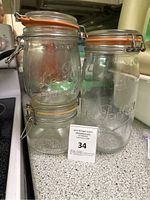 Photo showing three clear glass kitchen storage jars with airtight orange rubber seals and metal latch closures, embossed with Le Parfait logo.
