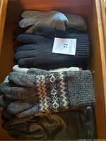Gloves and mittens in wooden drawer, showing different materials including knit, leather and fabric.