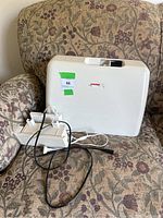 Front view of Janome sewing machine case with foot pedal and cords on patterned chair