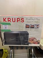 Boxed Krups ProChef Plus toaster broiler oven wrapped in plastic, showing brand and model details along with images of the appliance and food cooked with it.