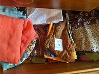 View of nine lightweight ladies scarves in assorted colors and patterns inside a wooden drawer