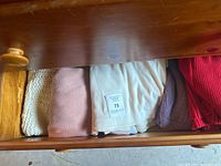 Drawer with various folded sweaters including cream chunky knit, pink plush, off-white, lavender, and red knit styles.
