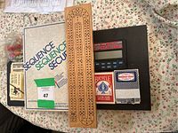 Lot arranged on floral tablecloth showing Sequence game box, wooden Cribbage board, calculator, and two decks of Bicycle playing cards