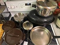 Photo of assorted pots and pans on stovetop including frying pan, covered pot, oval roasting pan, and saucepan.