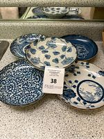 Five Japanese blue and white ceramic plates arranged on a countertop showcasing various traditional floral and wave designs