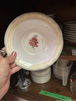 Front of a small shallow china plate showing beige-yellow scalloped edge and pink floral center design