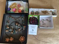 Photo showing multiple jewelry sets including a gold-tone flower necklace and earrings, necklace with clear and blue stones, turquoise coral set, red brooch, and pastel bracelet and earrings