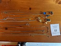 12 delicate vintage costume jewelry necklaces laid out on wooden surface, showing variety of pendants and chain styles.