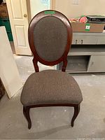 Front view of a vintage wooden dining chair with oval cushioned back and padded fabric seat in neutral color.