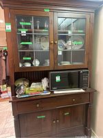 Photo of vintage wood hutch showing glass upper doors with displayed dishware and microwave on middle shelf.