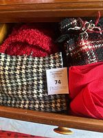 Four women's winter scarves displayed in a drawer featuring different materials and patterns including knit, plaid, solid red, and houndstooth.