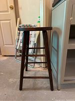 Side view of dark wooden barstool showing legs and footrests.